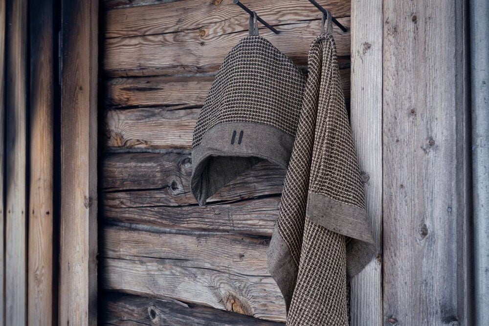 Musta ja beige saunahattu ja pyyhe koukussa.