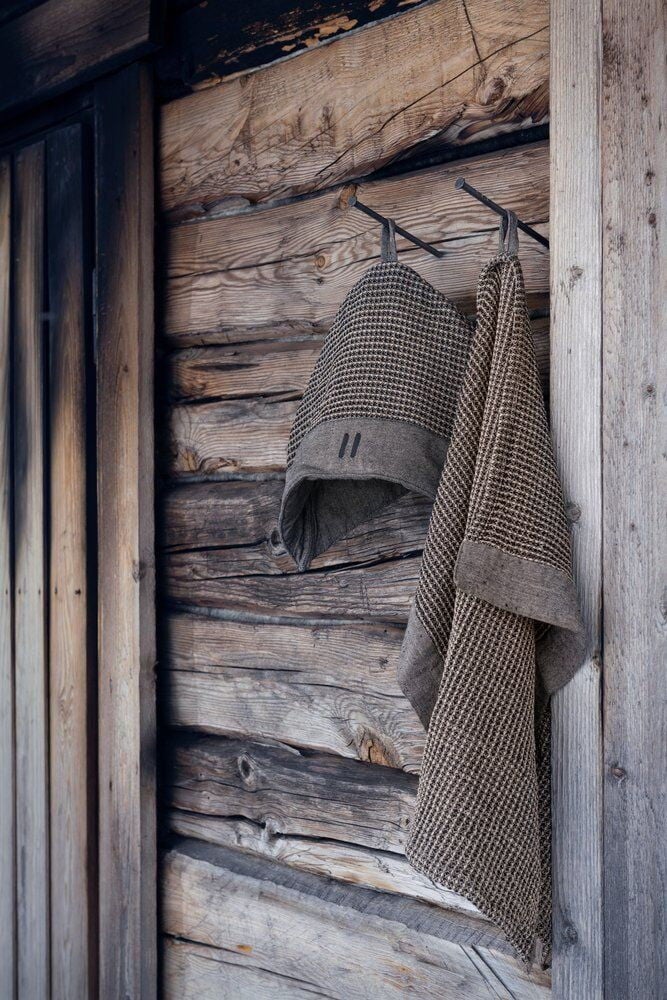 Musta ja beige saunahattu roikkuu puuseinällä.