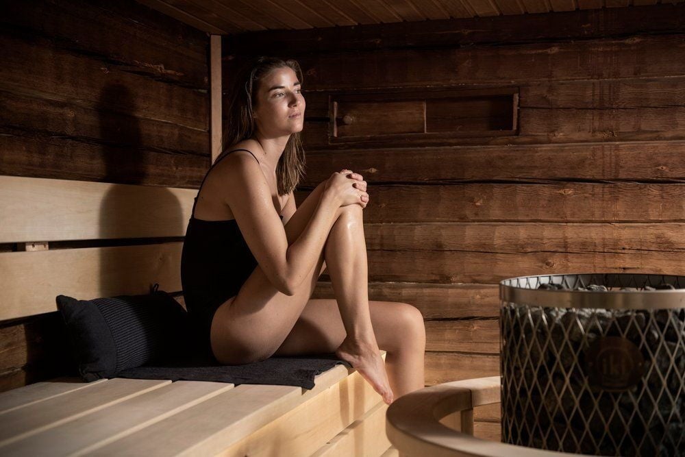 Nainen istuu saunanpenkillä mustan saunatyynyn kanssa.