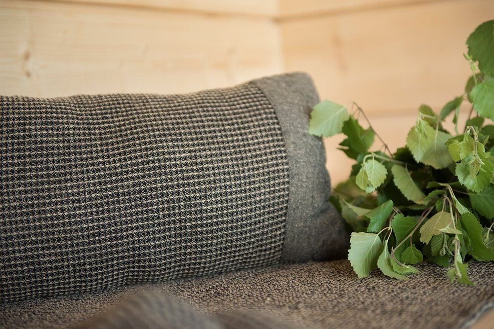 Musta ja beige saunatyyny puupenkillä koivunoksien kanssa.