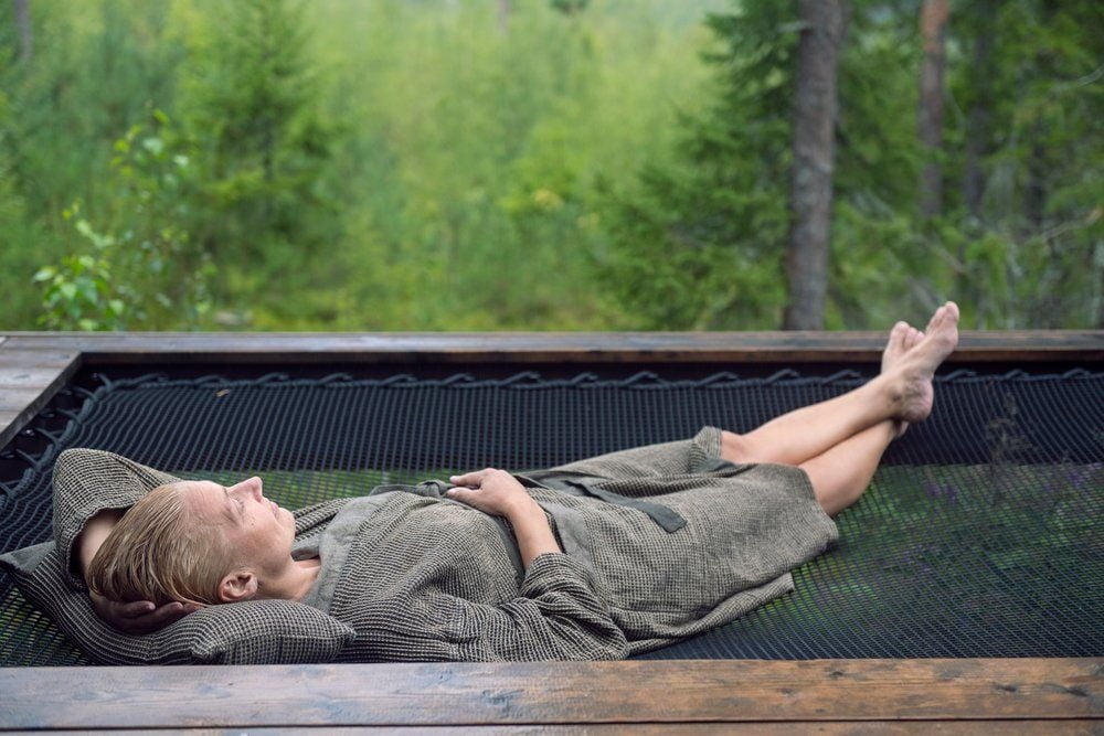 Henkilö makaa mustan ja beigen saunatyynyn päällä ulkona.