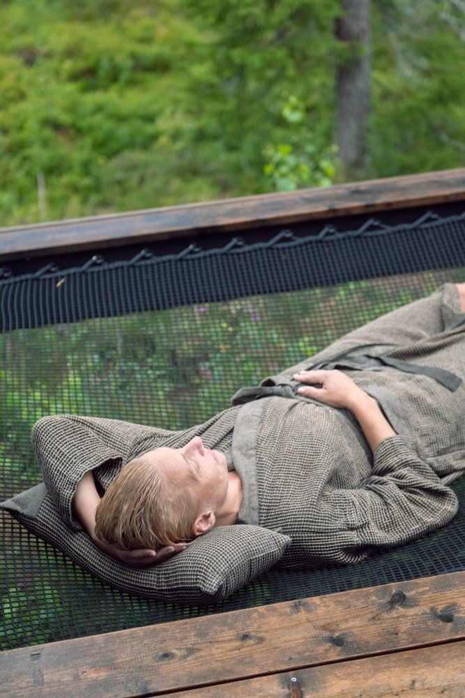 Henkilö makaa ulkona mustan ja beigen saunatyynyn päällä.