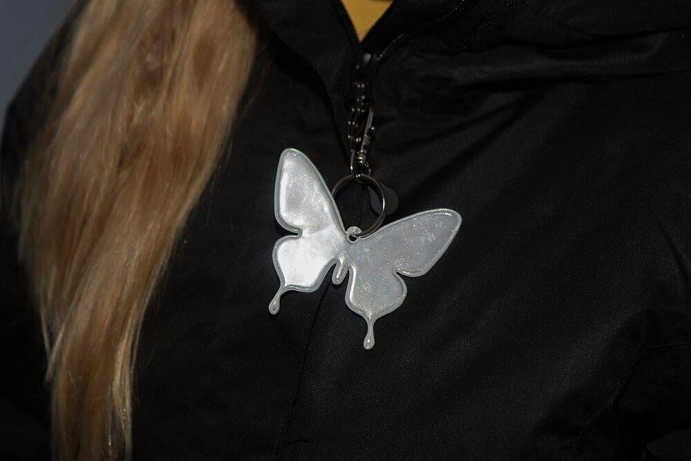 Perhosen muotoinen heijastin kiinnitetty mustaan takkiin.