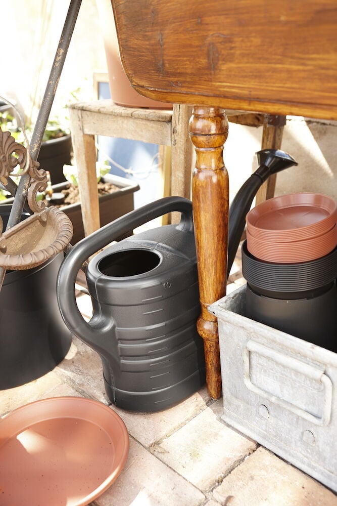 Musta kastelukannu, jossa on kahva ja nokka sisätiloihin.