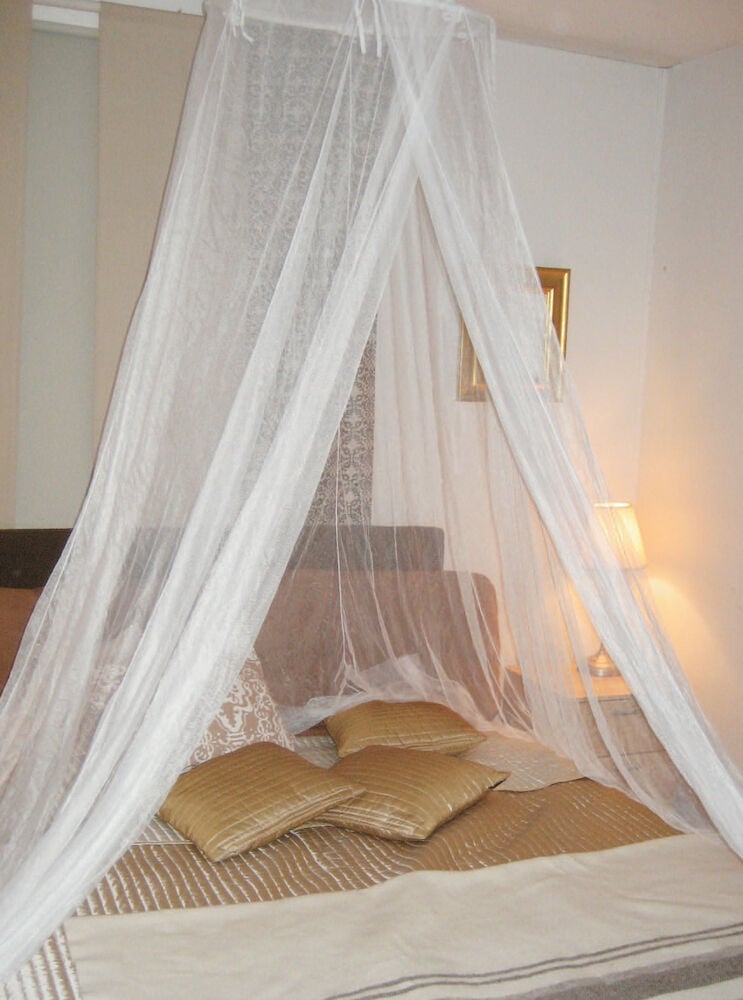 Valkoinen sängyverho pedatun sängyn kanssa, jossa on tyynyjä.