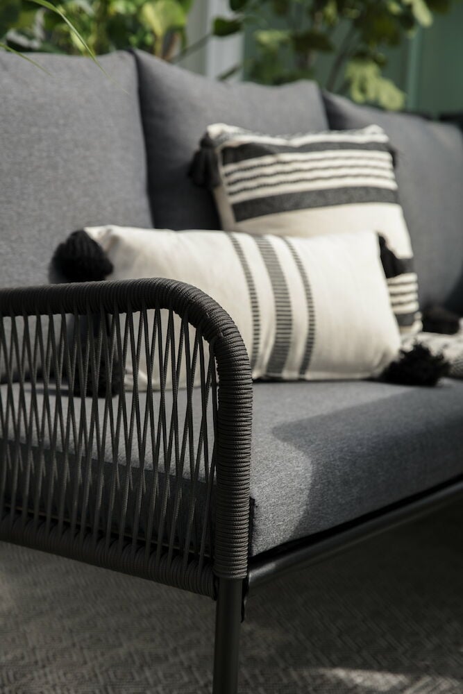 Musta oleskelusohva ulkokäyttöön koristeellisilla tyynyillä.