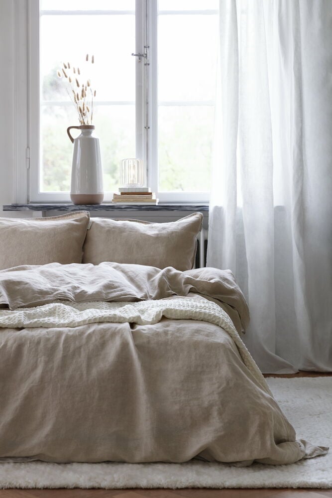 Handvävd naturfärgad ullmatta under säng i ljust rum.