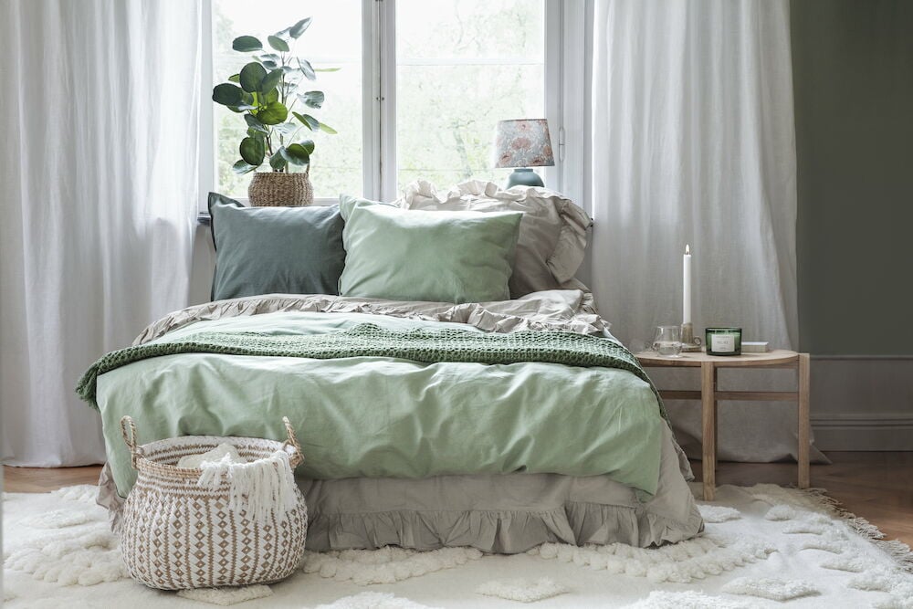 Vita gardiner i sovrum med grönbäddad säng.