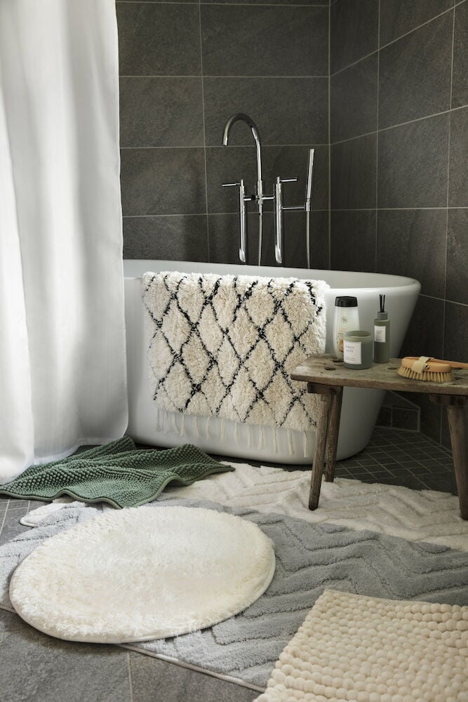 Beige badrumsmatta på klinkergolv framför badkar.