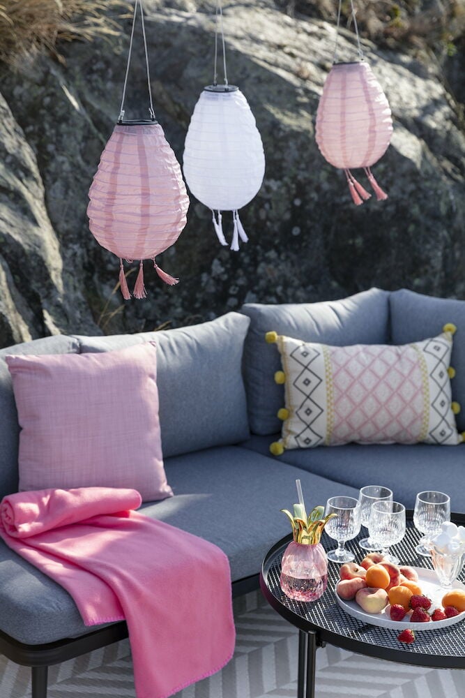 Harmaa ulkosohva, jossa vaaleanpunaiset tyynyt ja huopa.