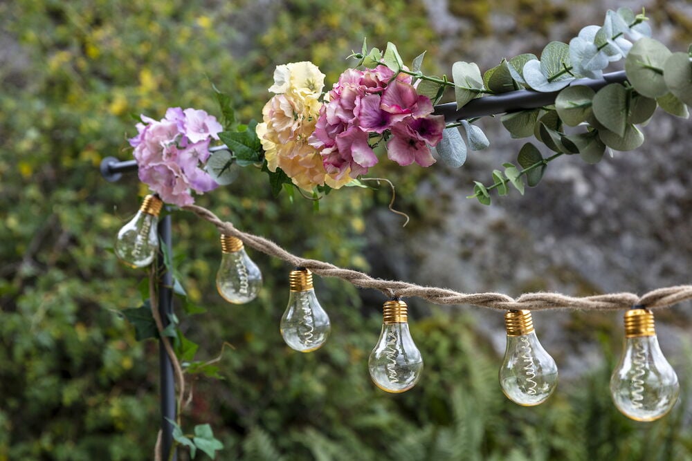 Harmaa teräsrakenne tekokasveilla ja valoketjulla.