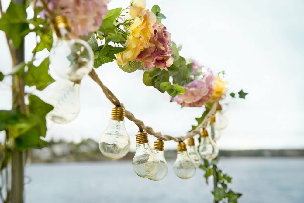 Harmaa koristeellinen teline valosarjalla ja tekokukilla.