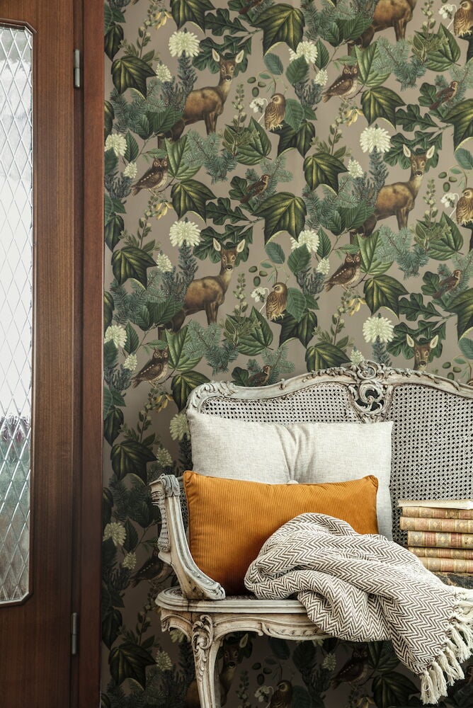 Blommig tapet med hjortar bakom antik fåtölj och kuddar.