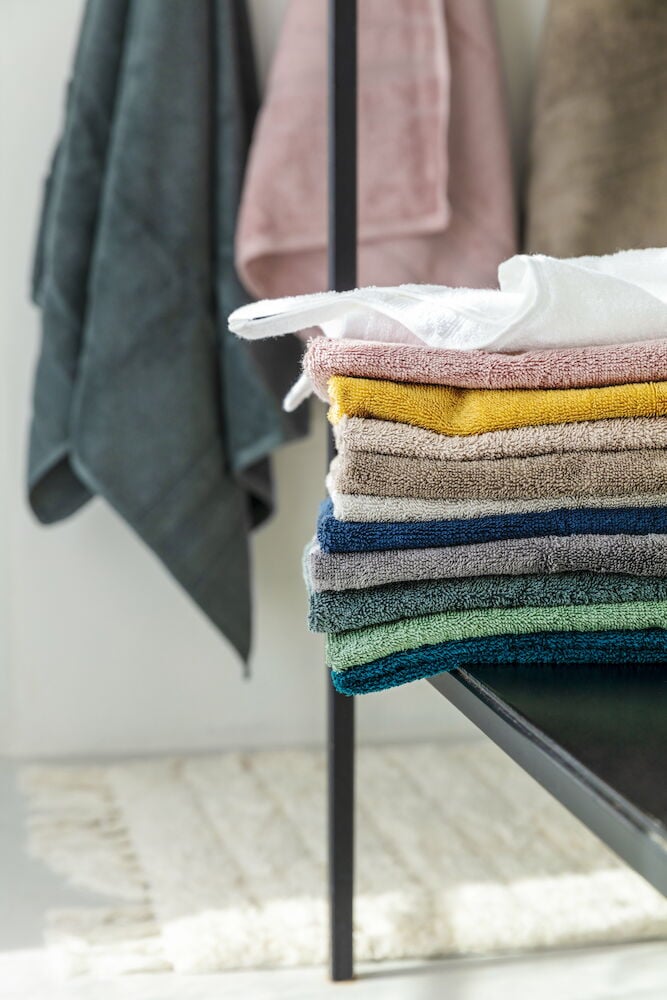 En vikt isgrön bomullshandduk på hylla.