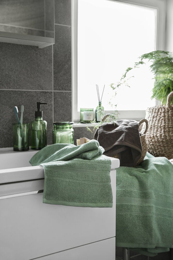 Grön badhandduk i bomull på vit badrumskommod.
