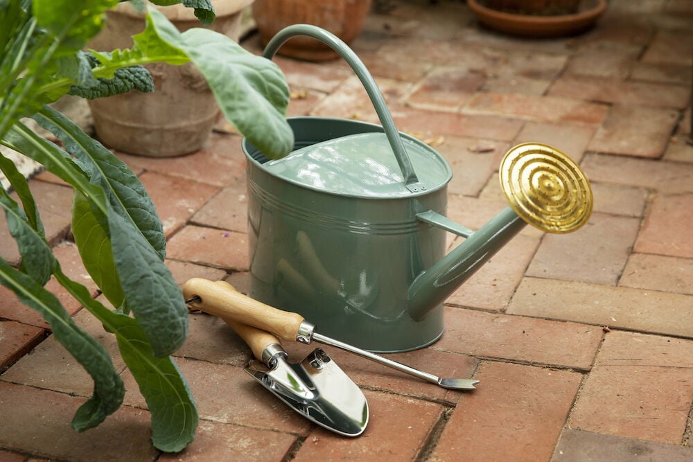 Grønn plantespade og vannkanne på teglsteingulv.