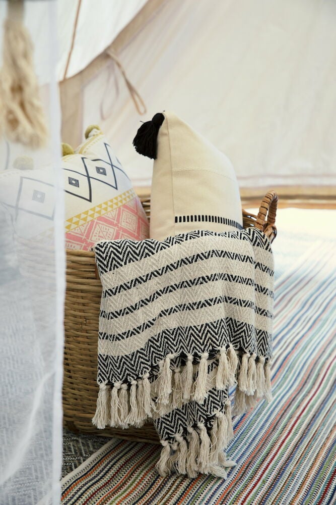 Eine cremefarbene Baumwolldecke mit Fransen im Korb.