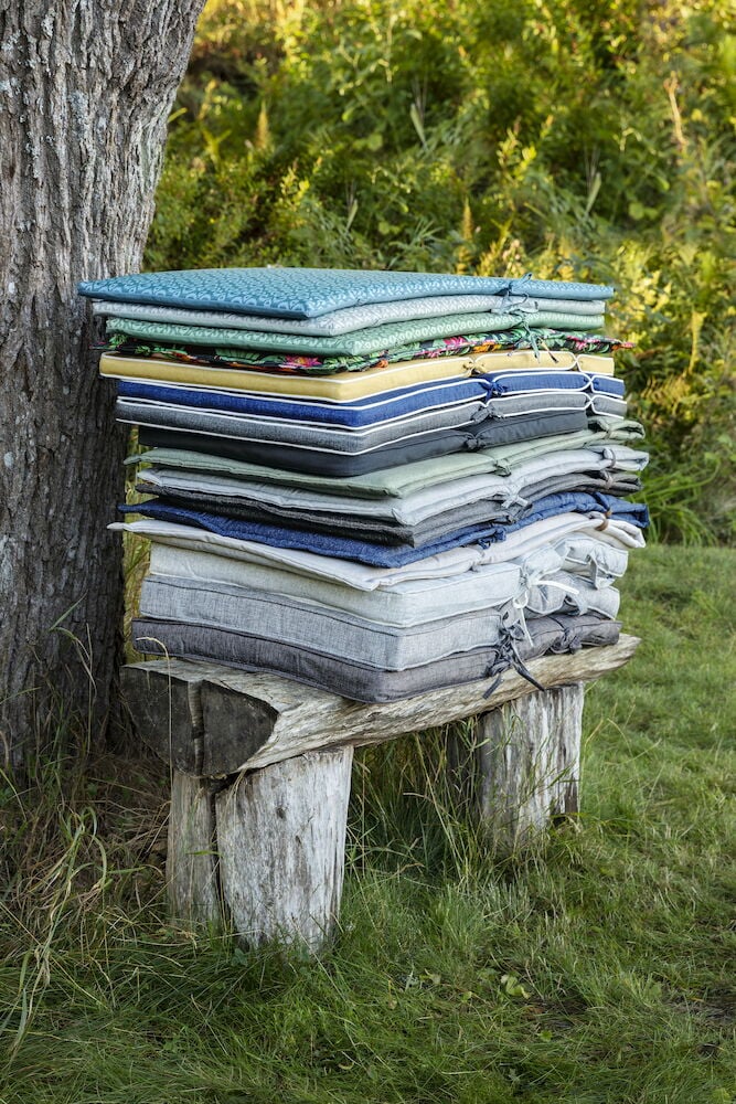 Stapel av trädgårdsdynor på bänk utomhus.