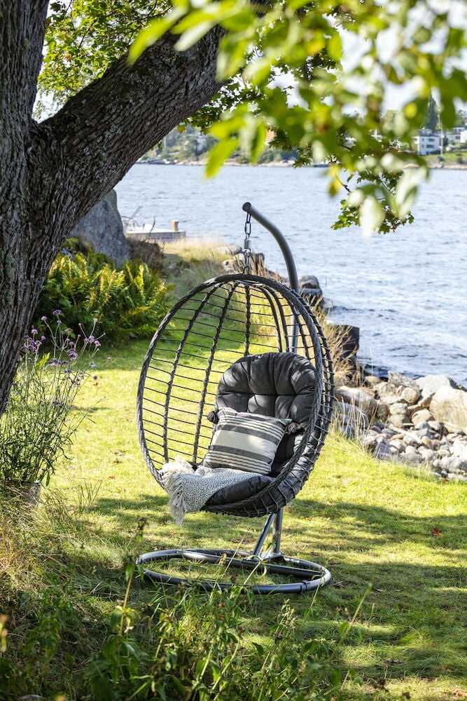 Tummanharmaa riippukeinu tyynyllä ulkona veden äärellä.