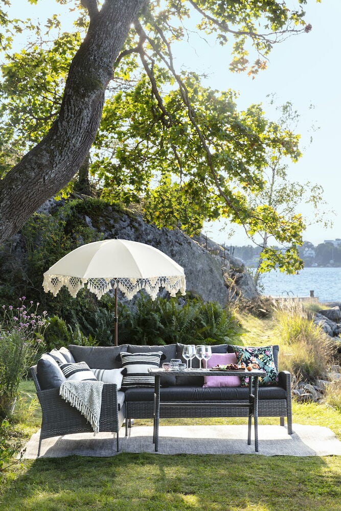 Vit parasoll med fransar över uteplats vid sjö.