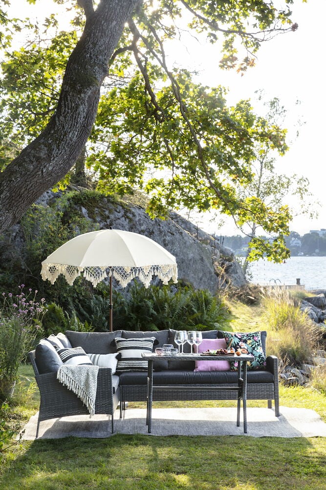 Vitt parasoll med dekorativa fransar i trädgårdsmiljö.