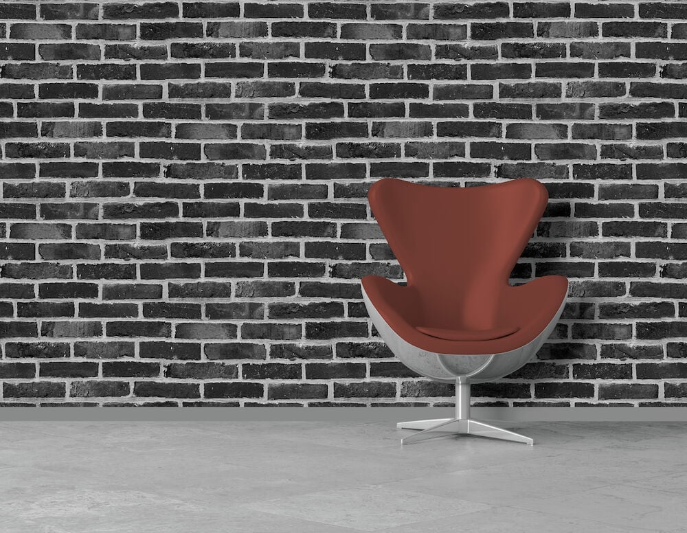 Svart tegeltapet och röd designfåtölj mot grått golv.