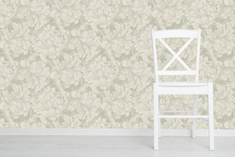 Vit stol framför grön bladmönstrad tapet.