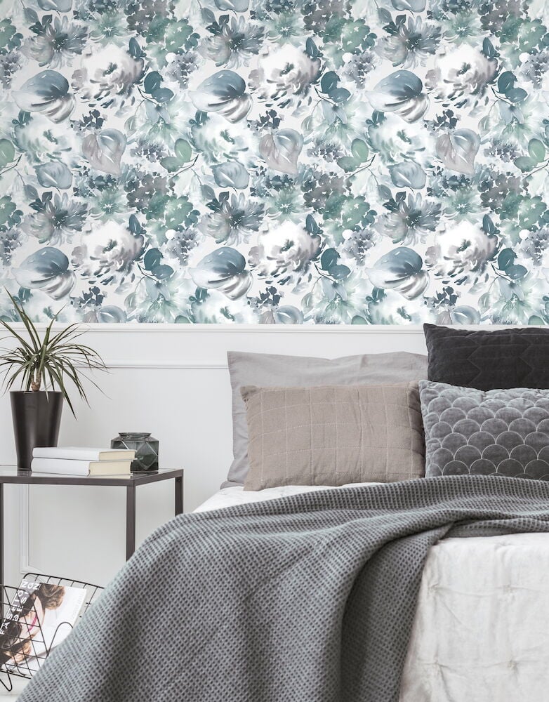 Grön blommig tapet bakom säng med gråa kuddar.