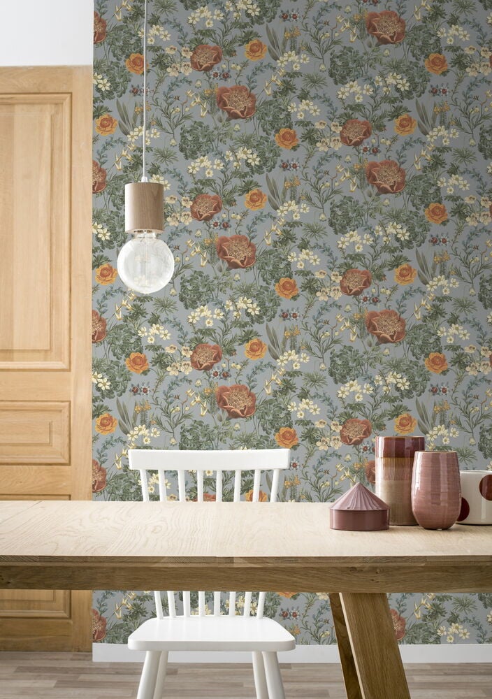 Sininen tapetti, jossa kukkaniittykuvio, puupöydän ja -tuolin takana.
