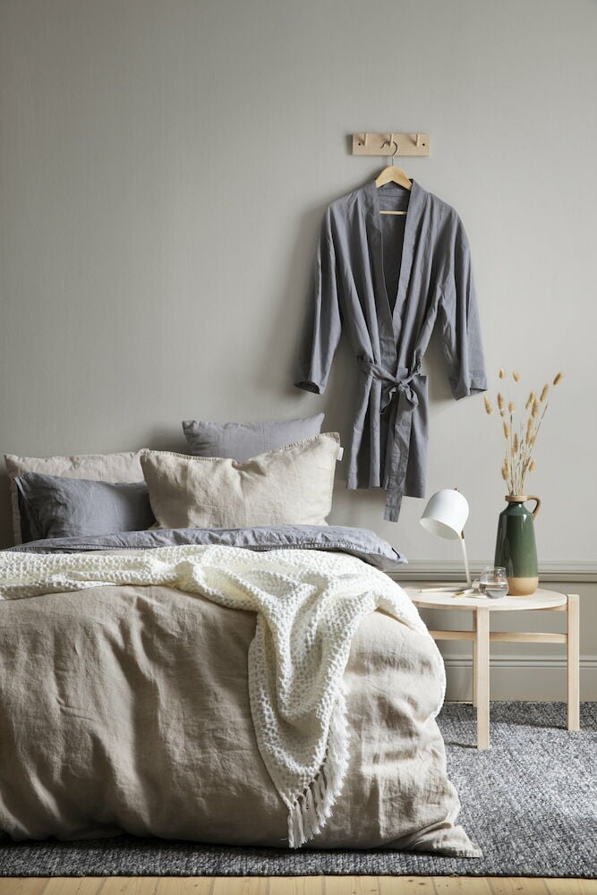 Grå håndvevd teppe under seng og nattbord.