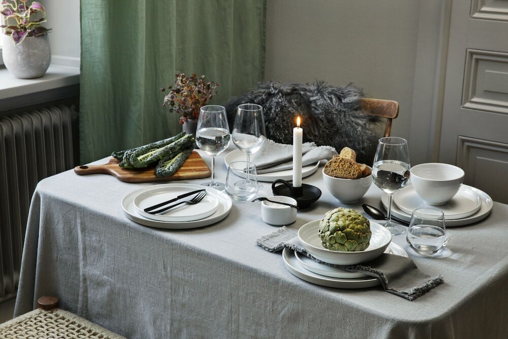 Vaaleanharmaa pöytäliina hapsuilla katetulla ruokapöydällä.