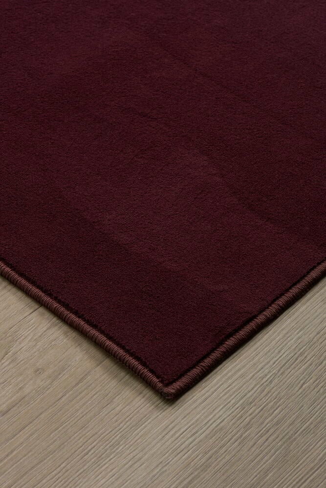 Vinröd matta på trägolv i närbild.