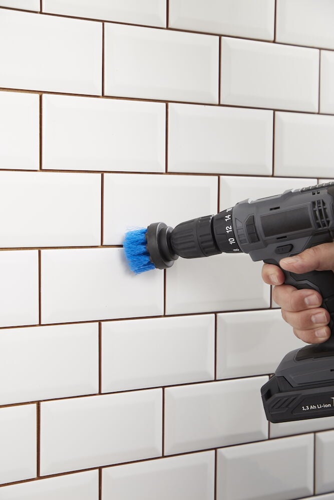 Blå borste på borrmaskin rengör vita kakelplattor.
