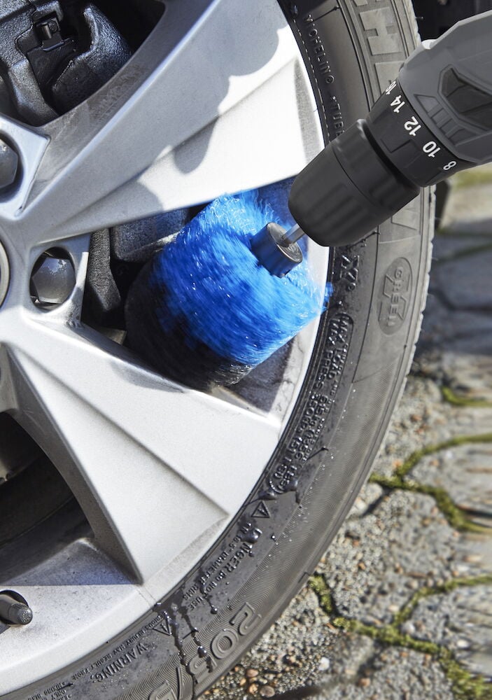 Blå rund borste rengör silverfärgad bilfälg.