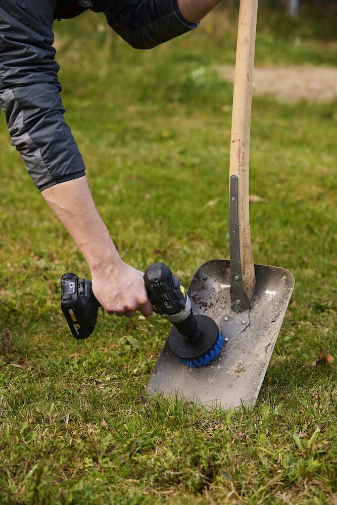 Person rengör spade med borstfäste på skruvdragare.