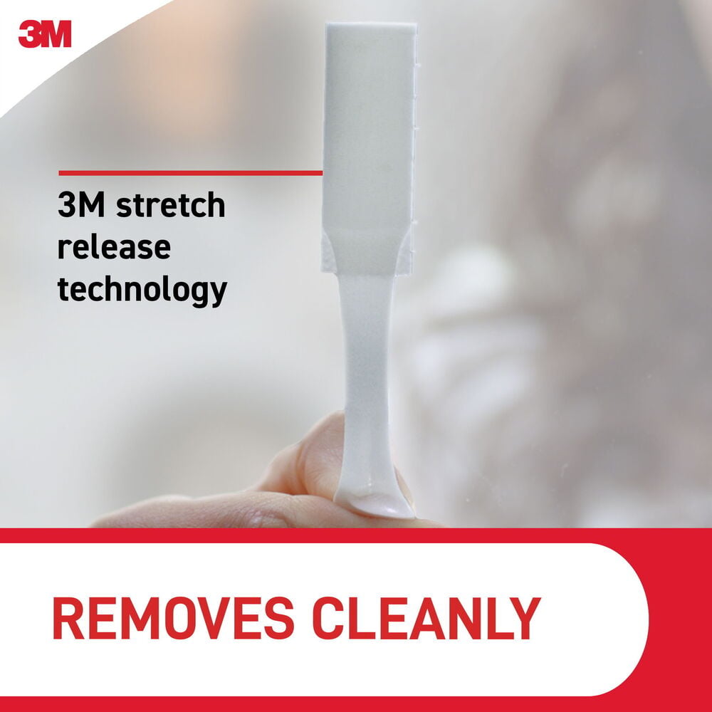 En hand sträcker en vit Tavelmonteringsstrips Command Large, visar stretch release-teknik.