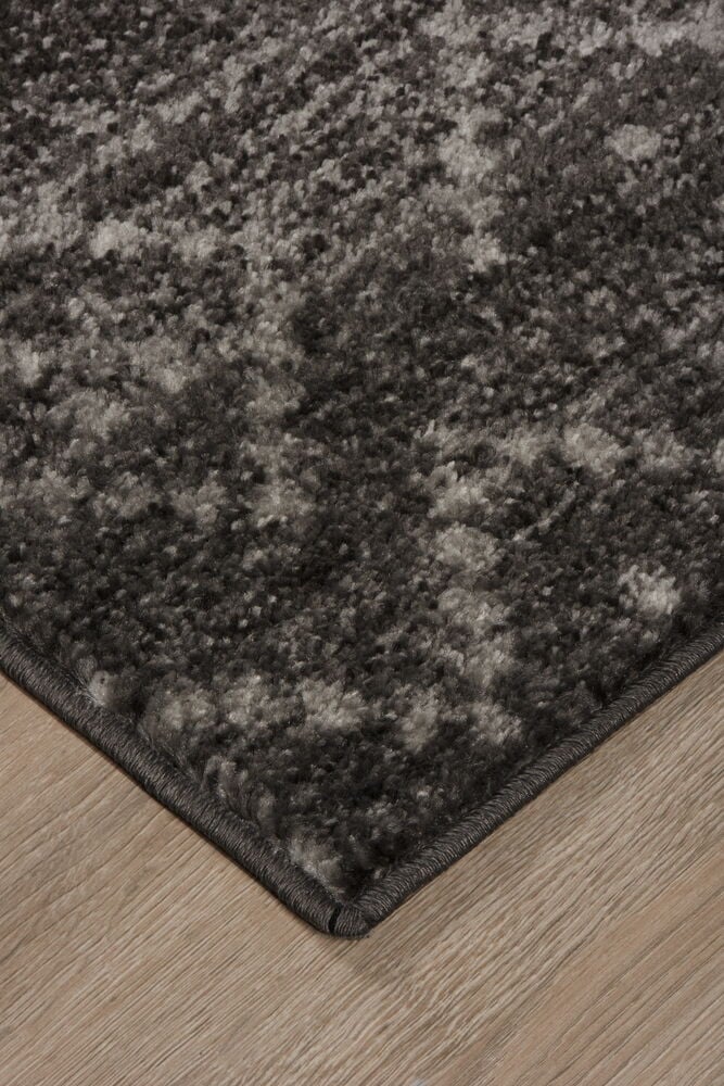 Die Ecke eines dunkelgrauen Teppichs auf Holzboden.