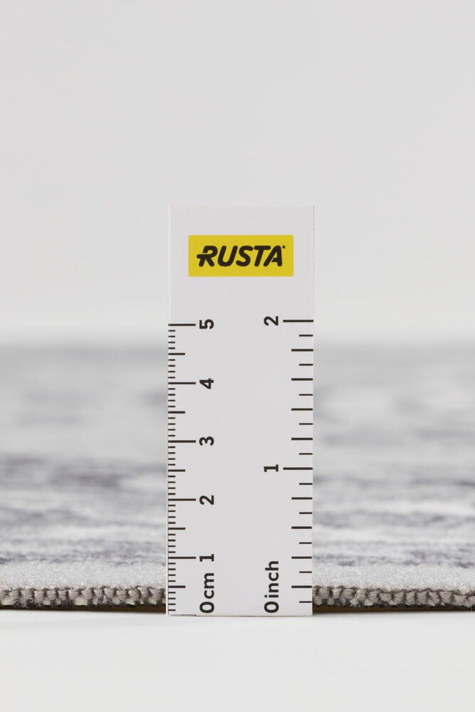 Nærbilde av grått polyamidteppe Lia med linjal som måler tykkelsen.
