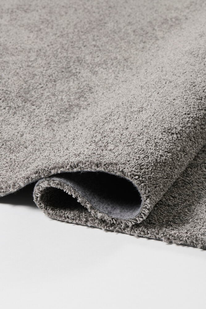 Mörkgrå matta Lizette i polypropen, delvis ihoprullad, som visar dess textur och undersida.