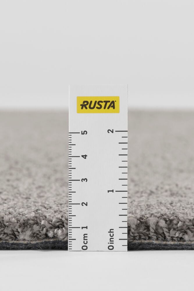 Närbild av en mörkgrå polypropenmatta med linjal som visar dess tjocklek.