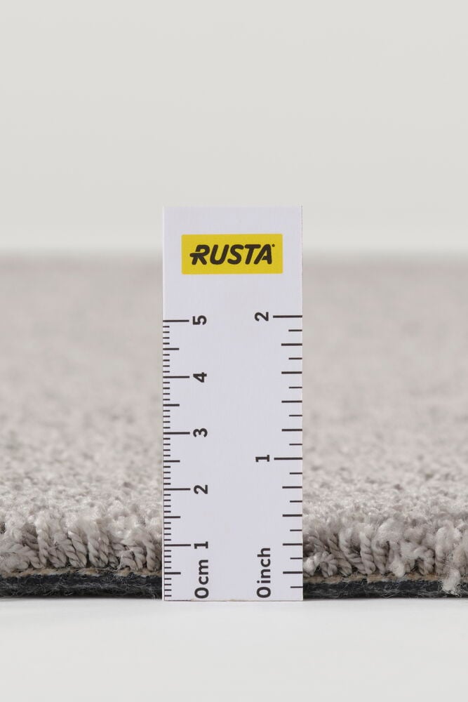 Lähikuva harmaasta Matto Lizette polypropeenista, sen paksuus mitattu valkoisella viivaimella.