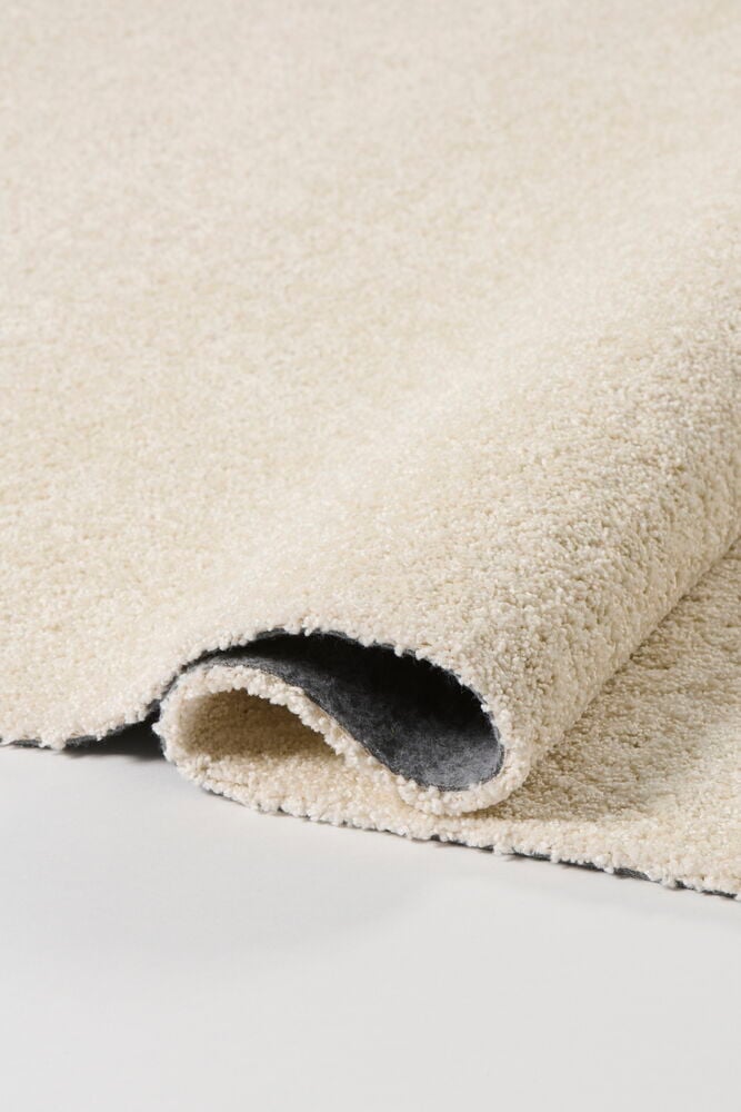 Naturfärgad Polypropen Matta Lizette, en ljusbeige ryamatta delvis rullad visar mörkgrå undersida.