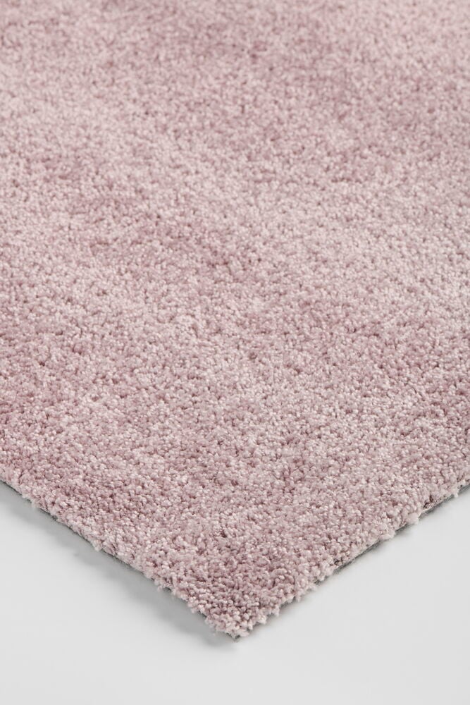 Närbild, snett uppifrån, av en rosa polypropenmatta med lugg och synlig baksida.