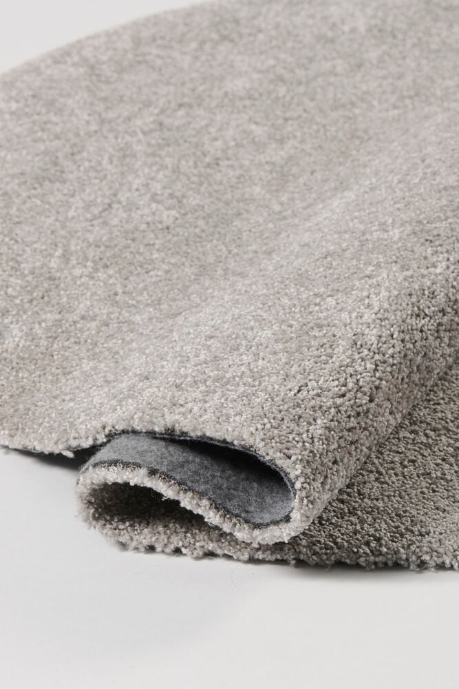Ein gerollter grauer Polypropylen-Teppich mit zotteliger Oberfläche und grauer Filzrückseite, Nahaufnahme.