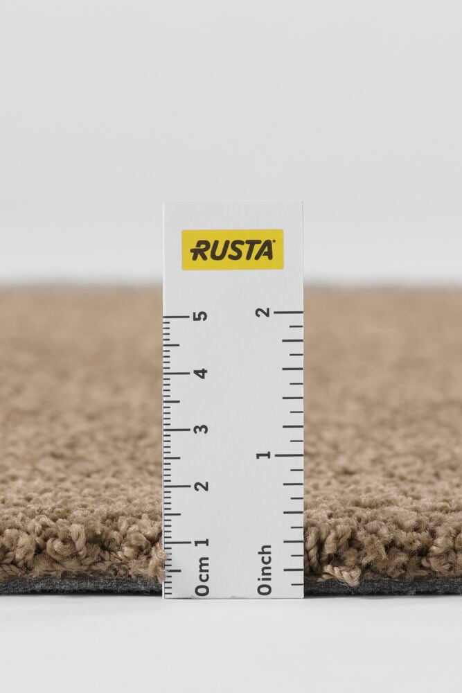 Nærbilde av et brunt polypropen Teppe Lizette med en hvit linjal som måler tykkelsen.