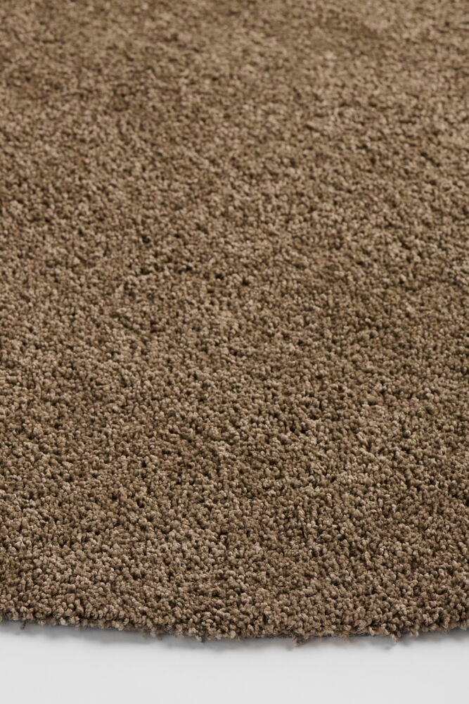 Nærbilde av et brunt Lizette-teppe i polypropen med teksturert lugg på hvitt underlag.