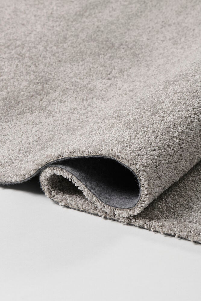 Harmaa kuvioitu polypropeenimatto on osittain rullattu, näyttäen sen tummanharmaan alapuolen.