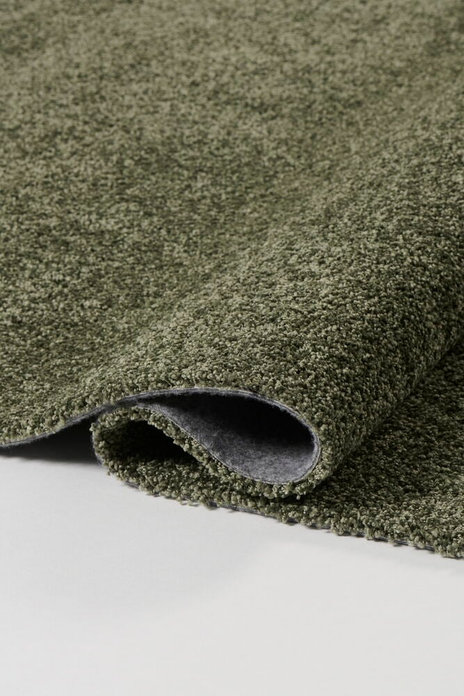 Vihreä kuvioitu Matto Lizette, osittain rullattuna näyttäen harmaan alapuolen valkoisella pinnalla.