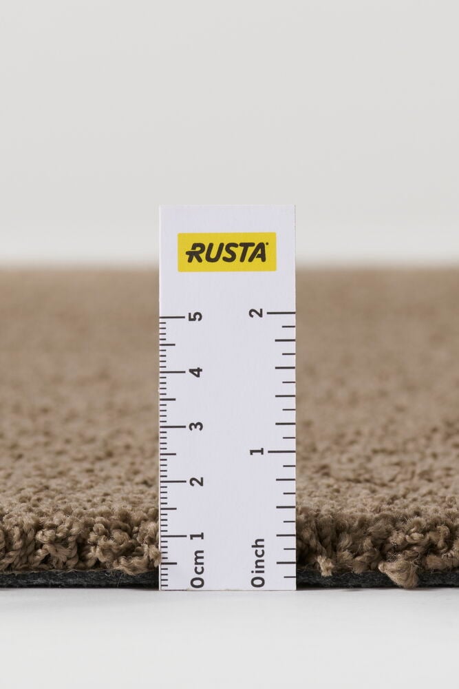 Närbild av en brun Lizette matta i polypropen med lurvig textur, mätt med linjal till ca 2 cm tjocklek.