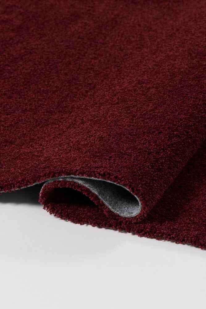 En vinröd matta av polypropen är vikt och visar sin grå baksida.